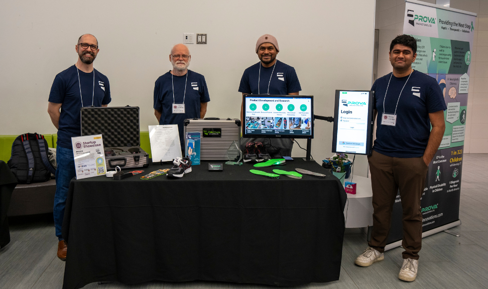 Four people standing behind a table. On the table are assistive mobility devices.