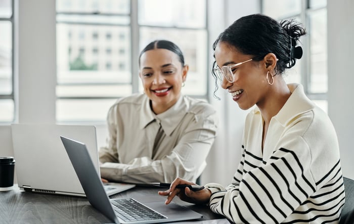 Two people smile while collaborating on a computer. 