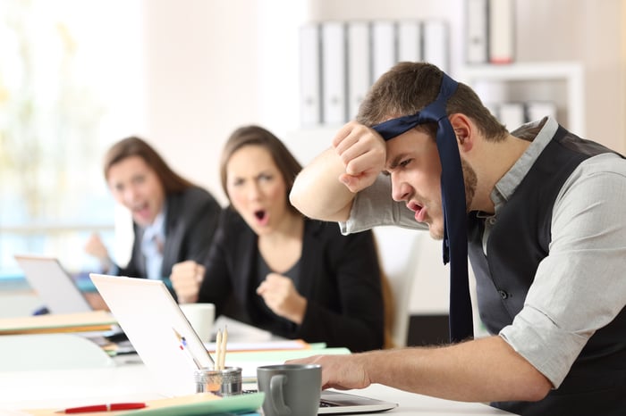 A lively office scene where an individual with a necktie wrapped around the forehead leans in with enthusiasm, accompanied by two animated colleagues at a desk.