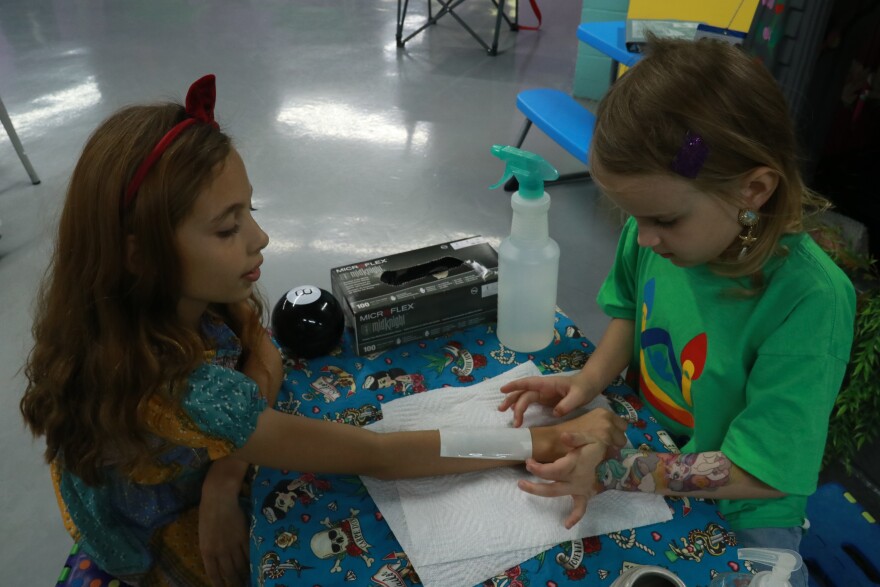 Kennedy Stanley, 6, practices a tattoo on Sophia Hubbard, 10, before helping her do tattoos on other children at Bouncers on 34th street, April 6, 2024. (Nicole Beltran/WUFT News)