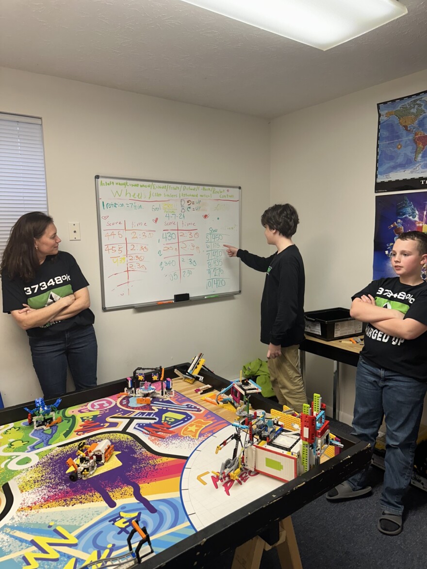 Parent mentor Liz Crawley with team behind the kid's art-inspired obstacle course as Liam Wiker points to past practice scores written on the board.