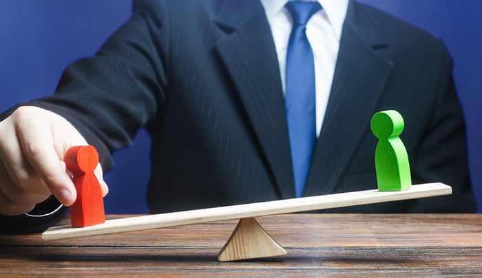 A person touches a red wooden piece on a seesaw while a green wooden piece is on the higher end.