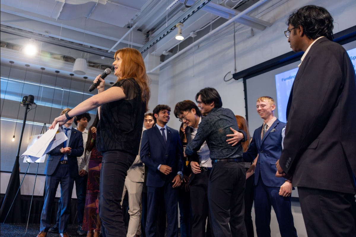 Woman announcing winners at Demo Day with groups standing behind her