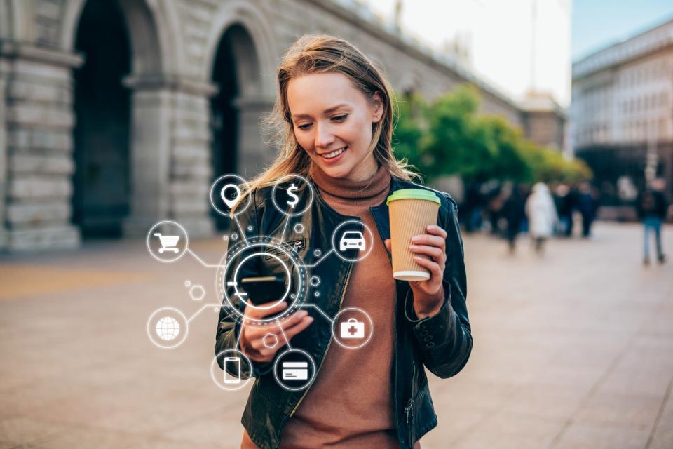 A person holds a coffee cup and a mobile phone with digital icons surrounding it.