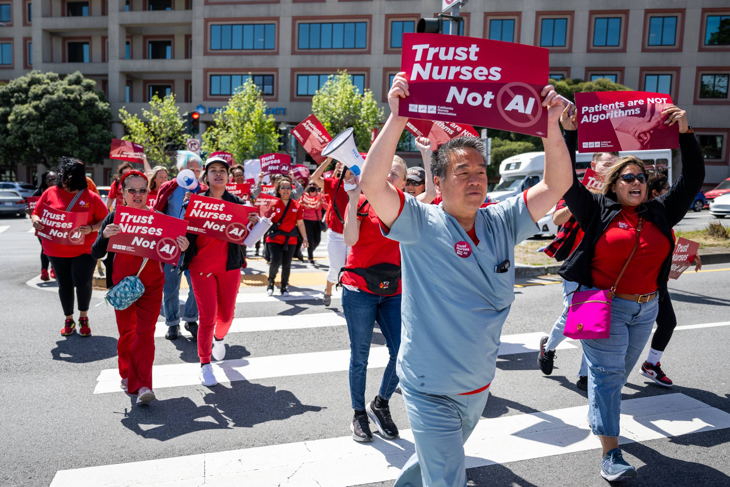 Many people dressed in scrubs hold red signs that say 