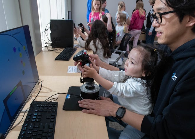 Senior research associate Beomyeong Park and his daughter Roha Park, 3, try out a psychomotor tool during the IHMC open house in Pensacola on Thursday, April 11, 2024.