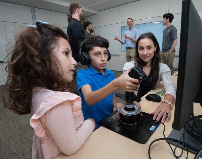 From right, research associate Emily Bowers helps Henrique Costa, 10, and Gabriela Costa, 6, try a psychomotor tool during the IHMC open house in Pensacola on Thursday, April 11, 2024.