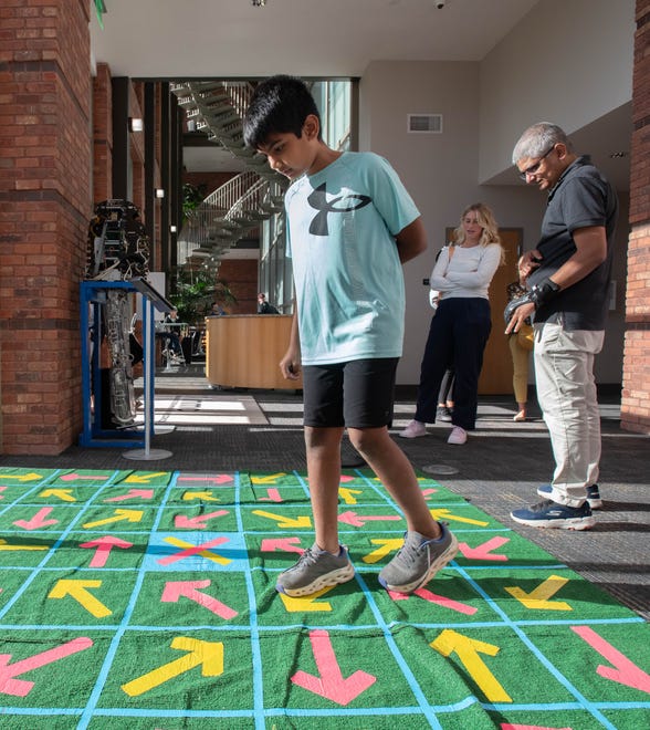 Tanay Kesharwani, of Pace, right, looks on as his son Srirama Kesharwani tries a Pensacola MESS Hall Archery Maze Challenge during the IHMC open house in Pensacola on Thursday, April 11, 2024.