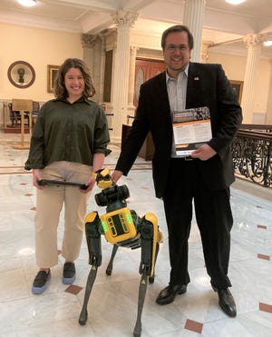 The Director of Human/Robot Interaction David Robert, left, pats Spot the robotic dog during its visit to the State House Thursday to champion legislation that would ban the weaponization of robotics and its use to hurt people or animals. Hannah Rossi, the field application specialist, left, was at the controls.