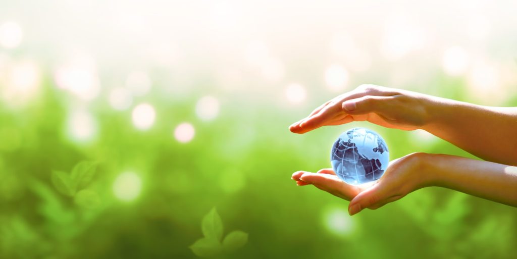 Image of a blue planet crystal glass globe ball in human hand on blurred green background.