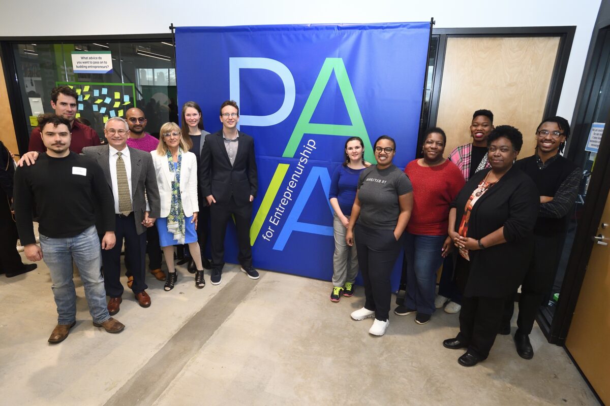 Two groups of people stand beside blue banner with "PAVA" in different colors and "for Entrepreneurship" in white text