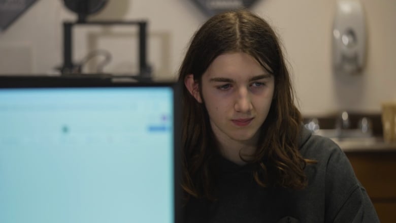 A boy with long hair, with part of his body covered by a computer screen