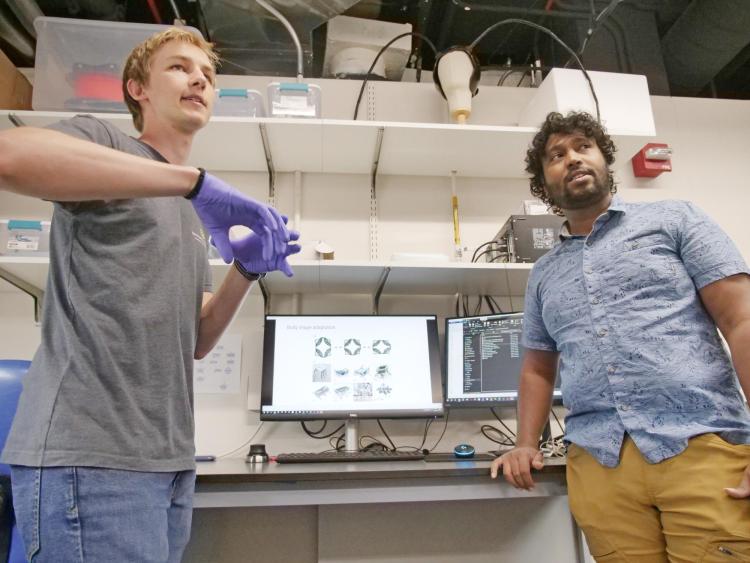 Two men stand on either side of a computer monitor