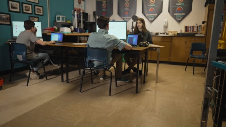 Three boys on computers at a table in a classroom