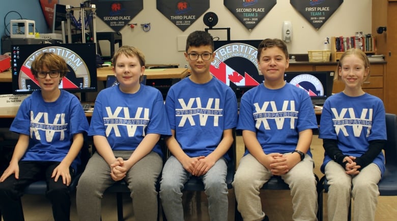 Five young kids sitting next to each other in a classroom. They all wear the same blue t-shirt.