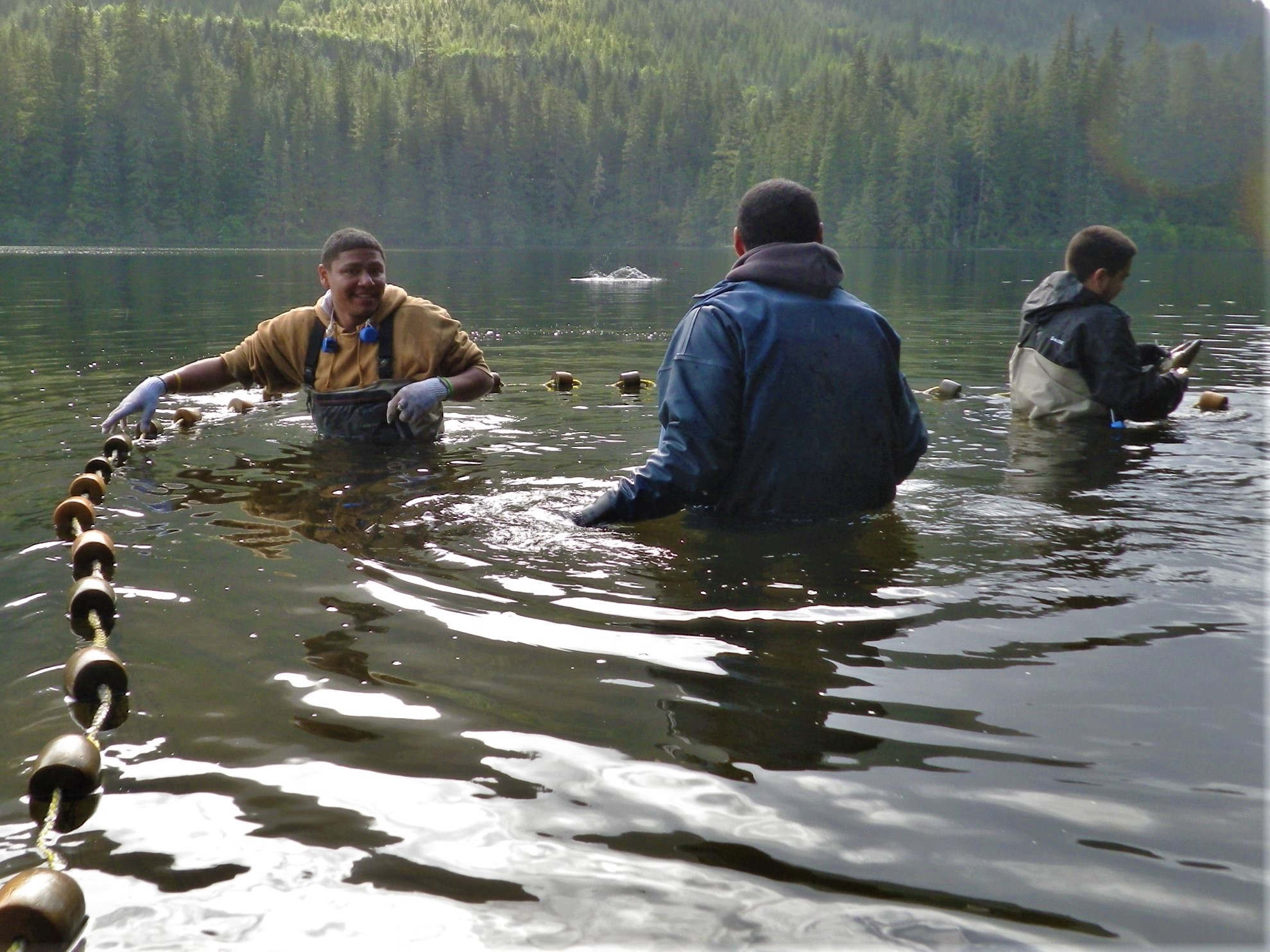 Youth in chest waders fishing near the forest.