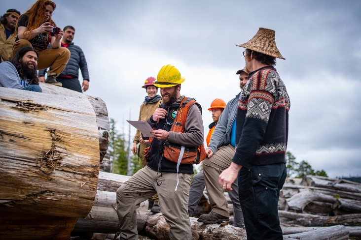 A small crowd of people smile while listening to someone talk in a timber area.