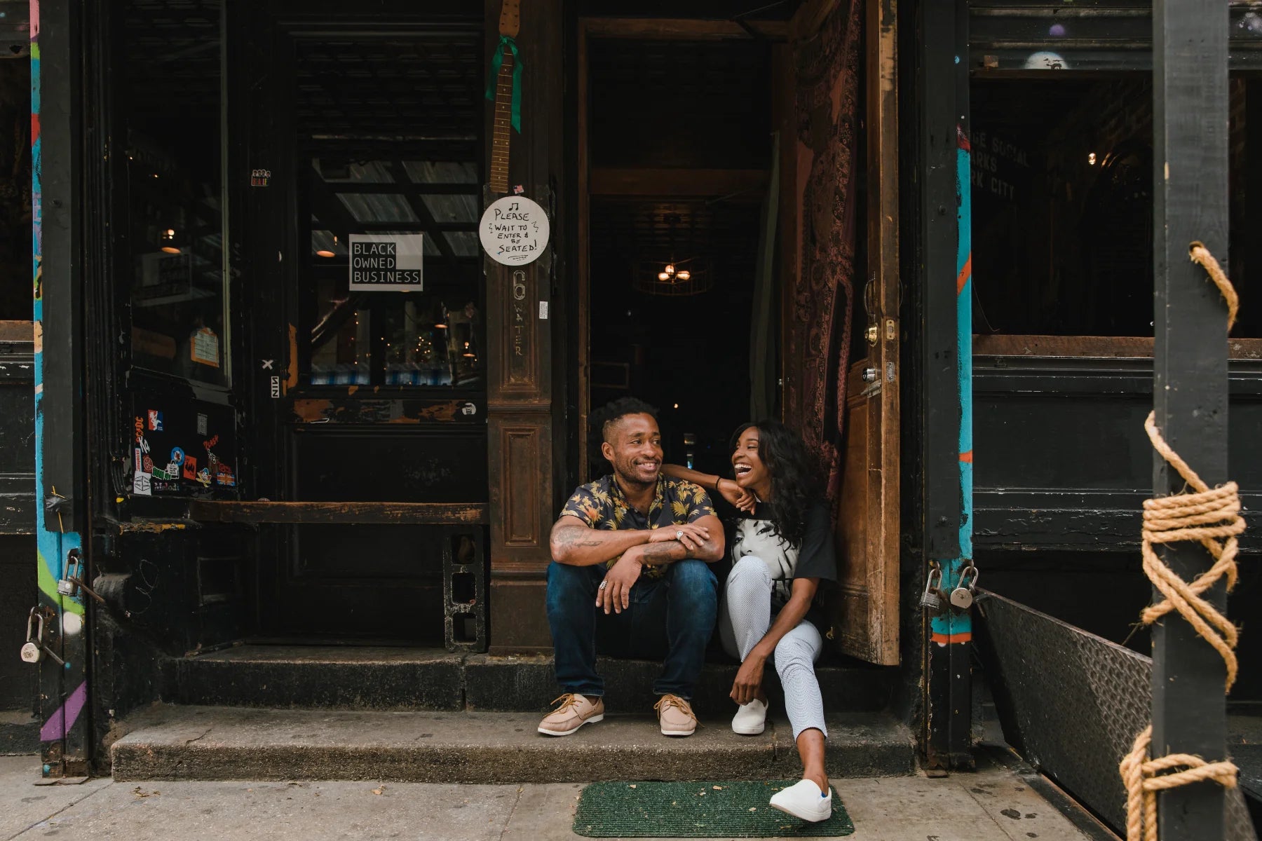 Two people sit on a stoop in front of a local business