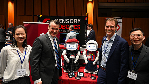 IU researchers and U.S. Sen. Todd Young pose with two small white robots.