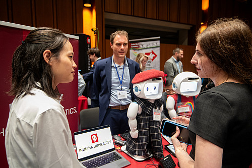 Three people talk over a table displaying a small white robot