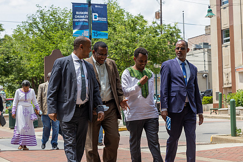 Four men walk down a city street talking