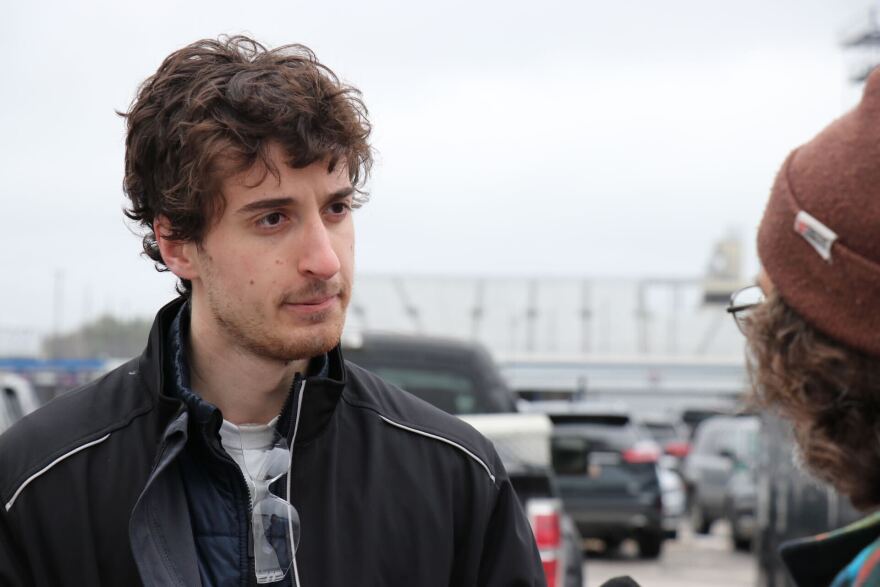 A white man looks at someone off camera who is talking to him. 