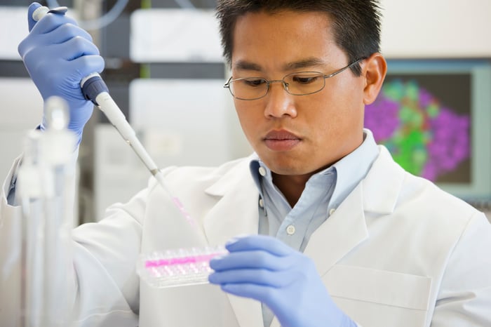 A lab technician using a pipette device to place liquid samples into a test tray. 