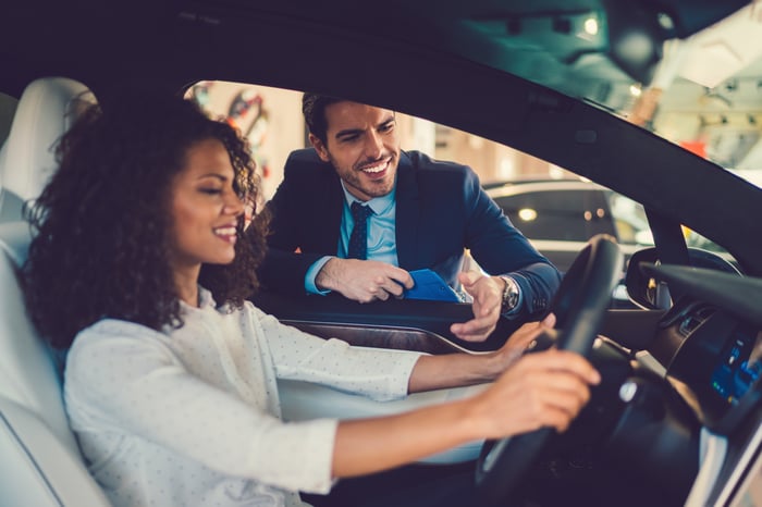 New car owner behind wheel of car with salesperson standing by driver-side door.