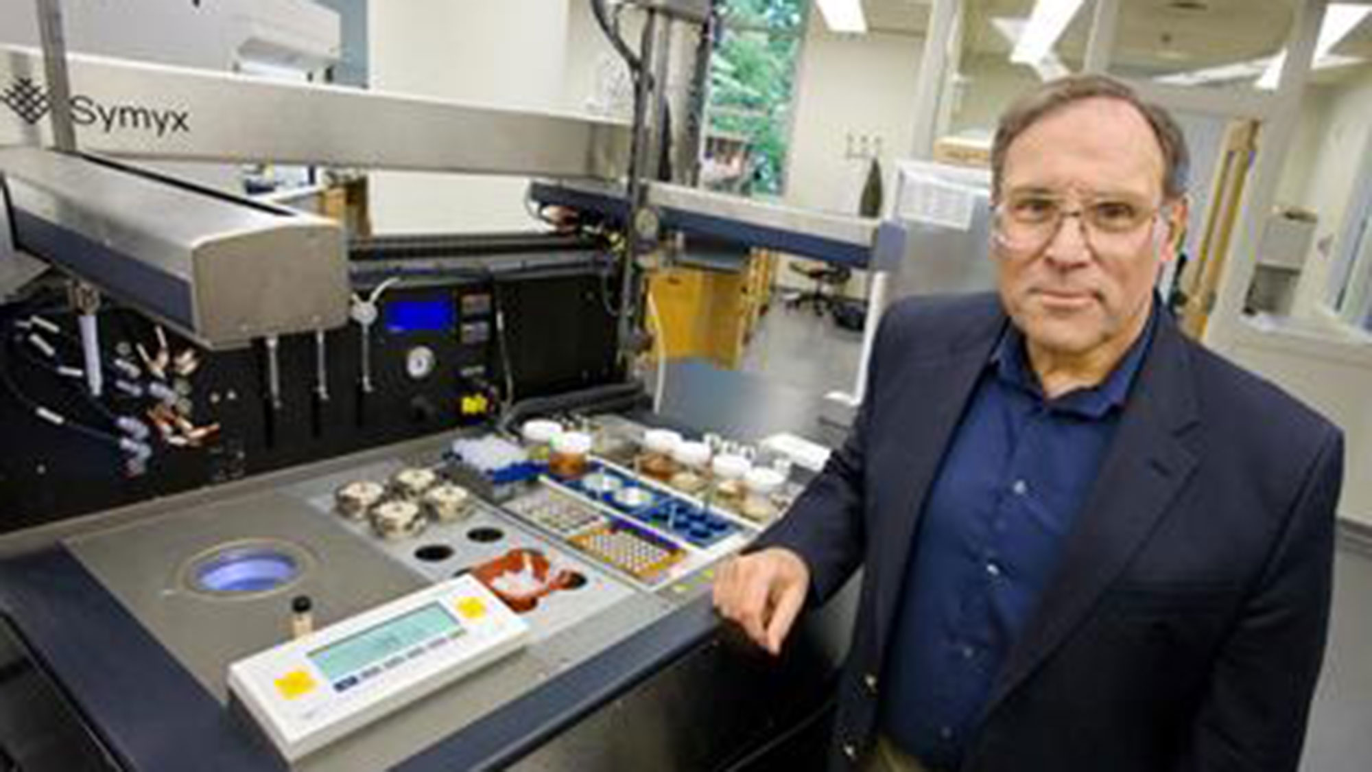 A person wearing a suit stands next to a chemical bench.