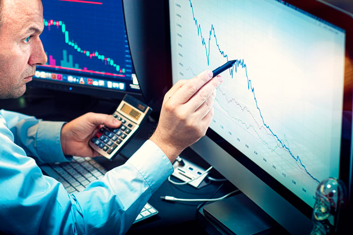 A professional money manager using a calculator and stylus to analyze a stock chart displayed on computer screen.