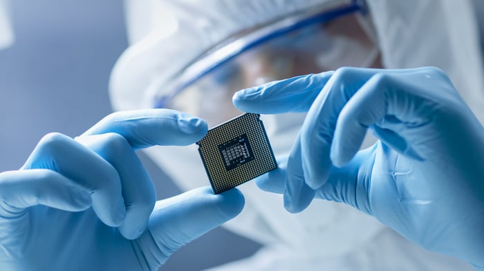 A person wearing gloves and a sterile full-body coverall who's closely examining a microchip in their hands.