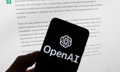 OpenAI logo on a phone in front of a computer screen displaying text