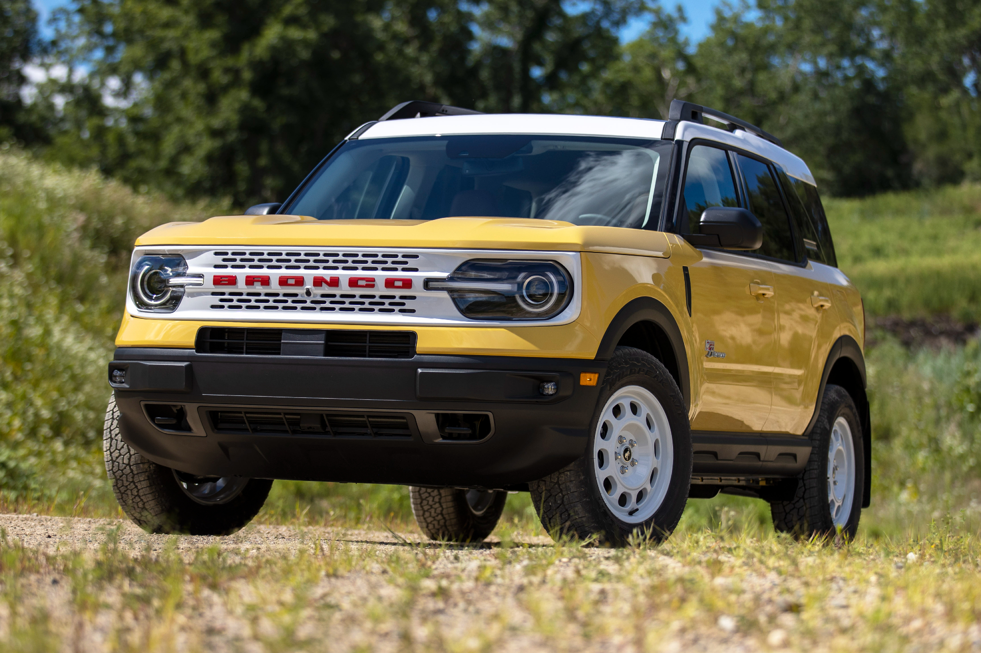 2023 Bronco Sport Heritage Limited Edition Yellowstone Metallic parked on a dirt road with grassy hills and trees in the background.