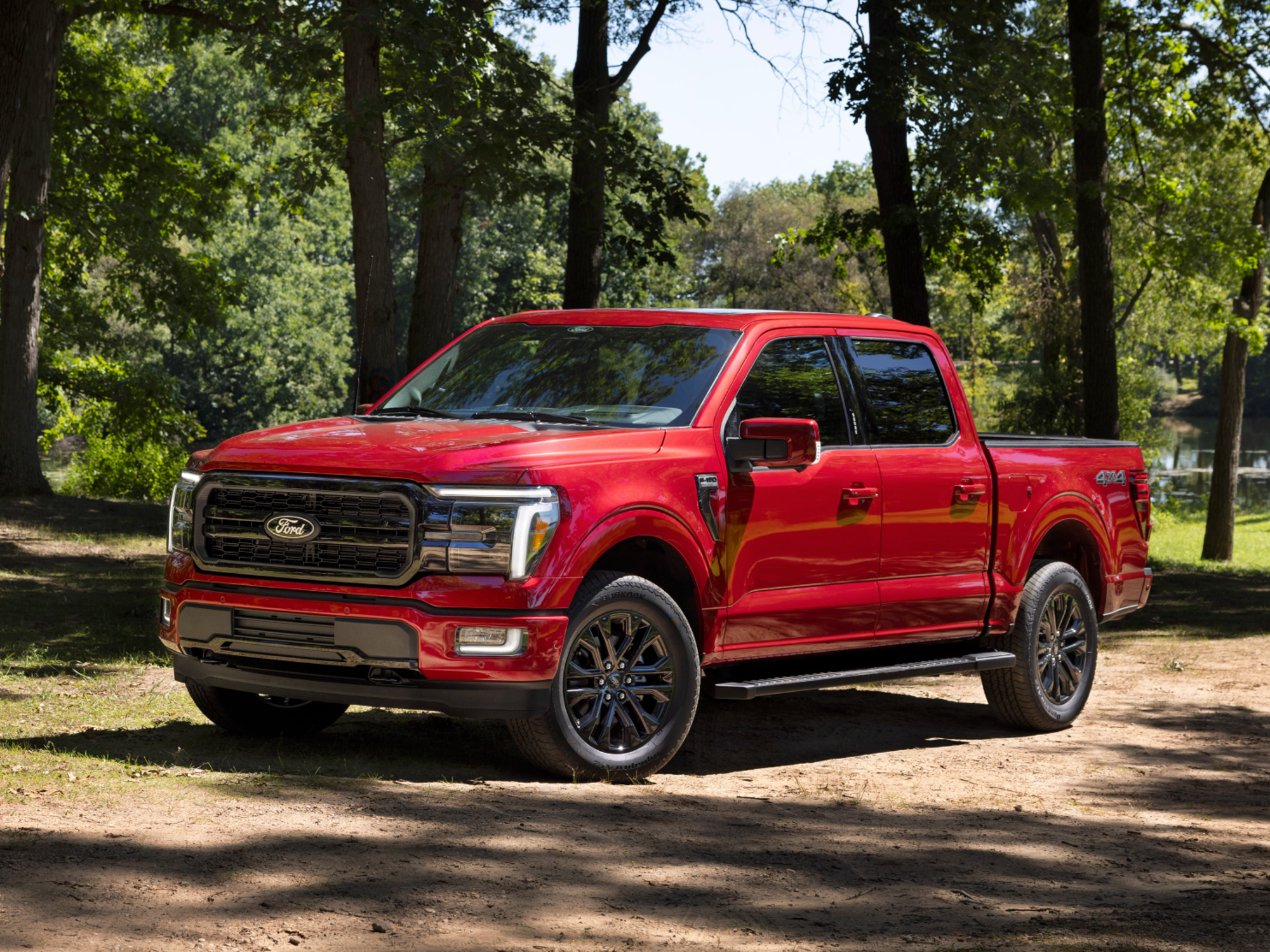 2024 Ford F-150 Lariat pickup truck front left three-quarter view parked on grass in front of trees.