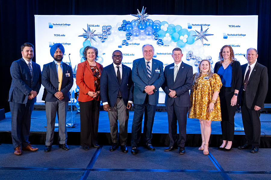 A group of nine people pose in front of a large backdrop to celebrate a ceremonial signing.