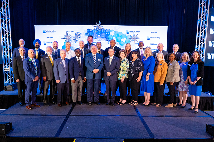 A large group of people stand on a stage and pose for a photo during a celebratory signing.