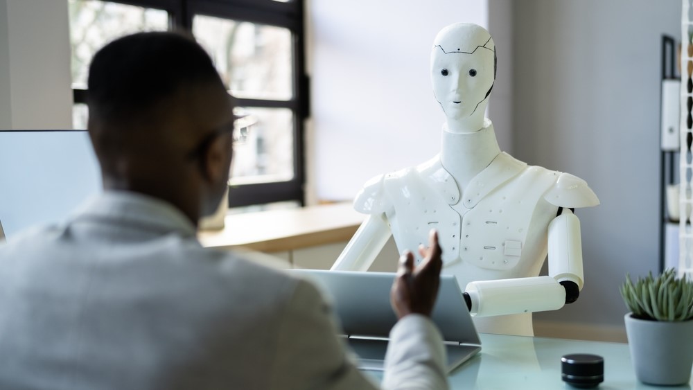 A robot sitting opposite a human who is gesturing with their hands.