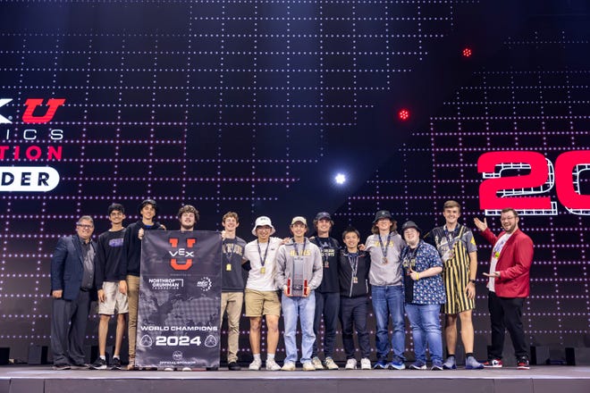 Purdue University's robotics team, Purdue SIGBots, Mihir Laud, Stephen Hohnholt, Joey Krejcie, Joe Lach, Brandon Liu, Dominic Holifield, Sean MacDonald, Alex Lam, Conner Siebert, Jacob Zawacki, and Max Johnson stand in between two VEX Robotics event organizer as they accept their championship banner, at the VEX Robotics World Championship, on April 30, 2024, in Dallas, Texas.