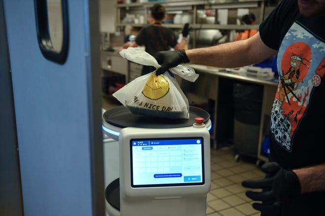 Owner Nathan Blais drops a carryout order onto Rosie the robot at Fai Thai in Knoxville, Thursday, May 23, 2024.