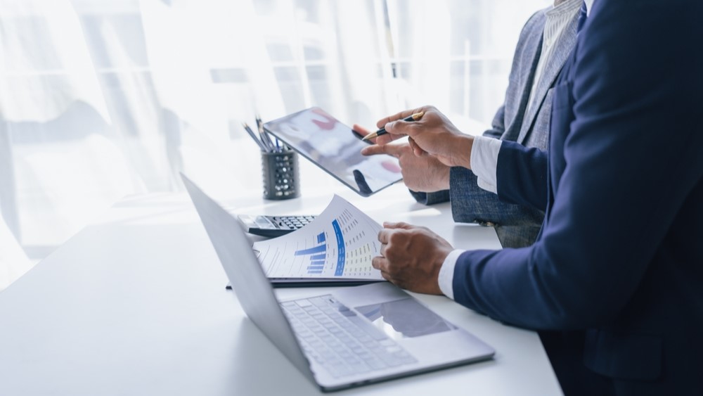 Two people look at a laptop and papers in an office setting.