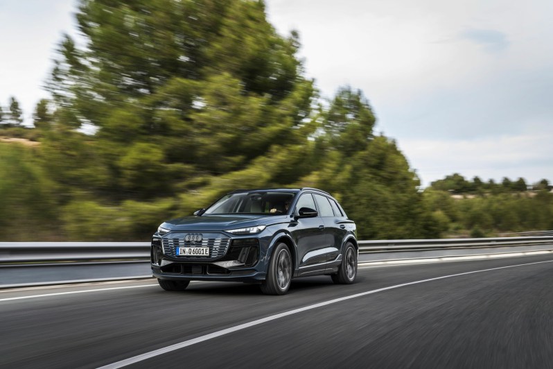 Audi Q6 e-tron driving on a highway with trees, land, and ocean in the background.