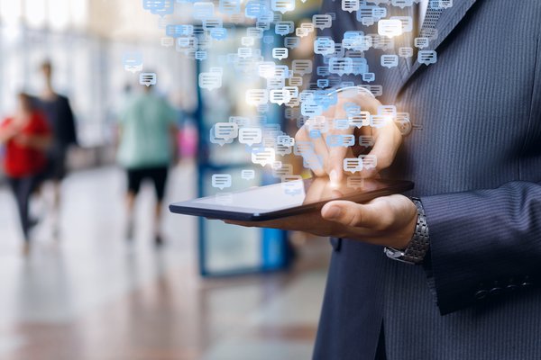 Person holding a smartphone with images of conversation bubbles seemingly floating above it.