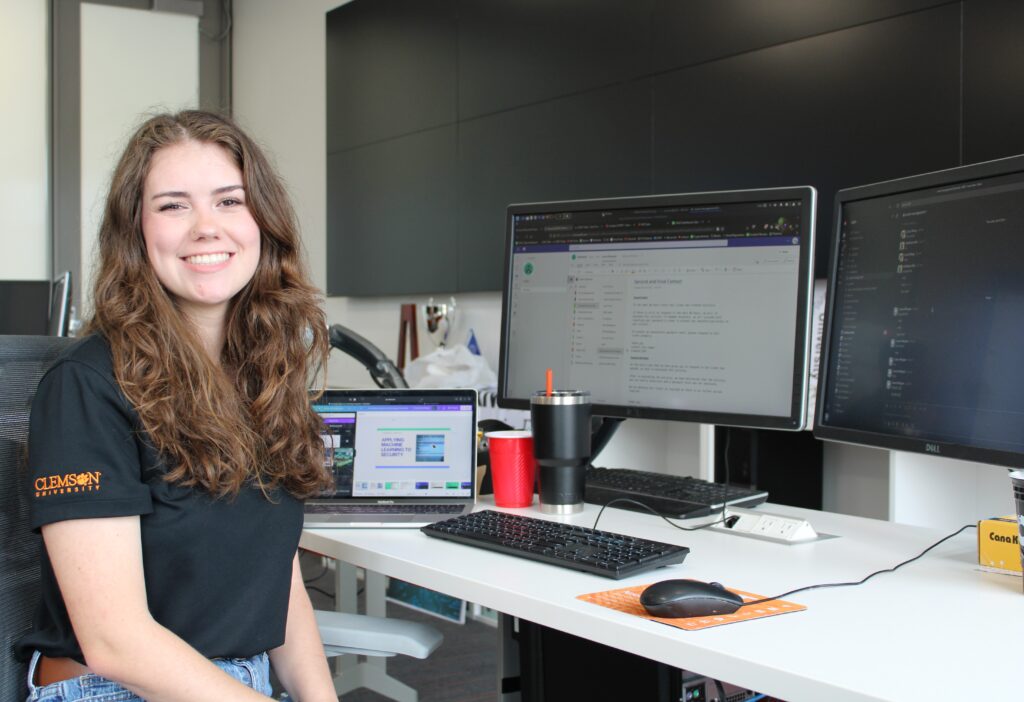 Laura Morgan sits in front of her desk with two computer screens and smiles.