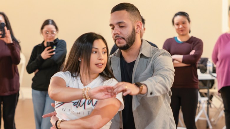 Young Latino couple dances as students watch on.