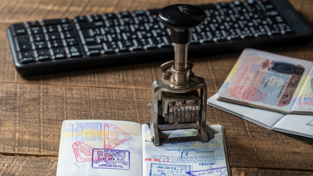 A stamp sits on a heavily stamped passport. There is another passport and a keyboard in the background.