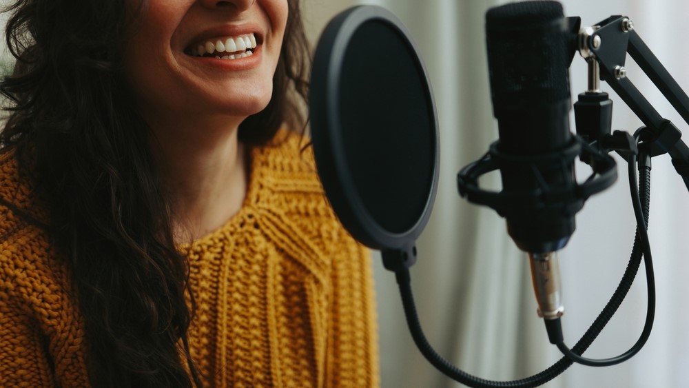 A woman sits behind a microphone, ready to record her voice.