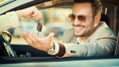 a smiling person sitting in their car holding their hand out the window to take keys off another person.jpg