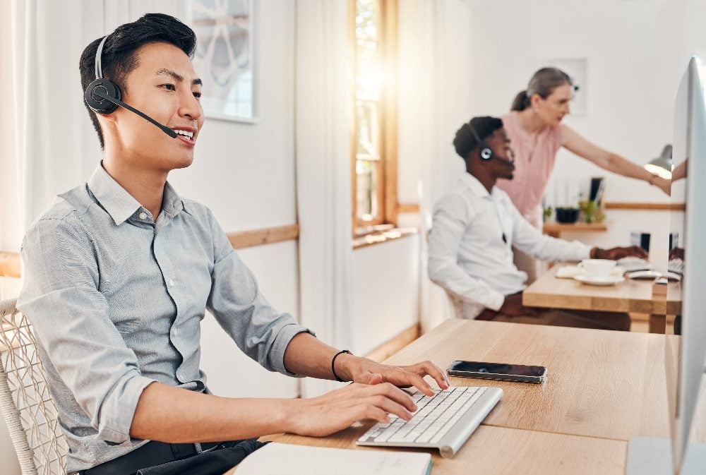 Customer support workers wearing headsets and working on computers in contact center in piece about enhancing customer support with analytics.