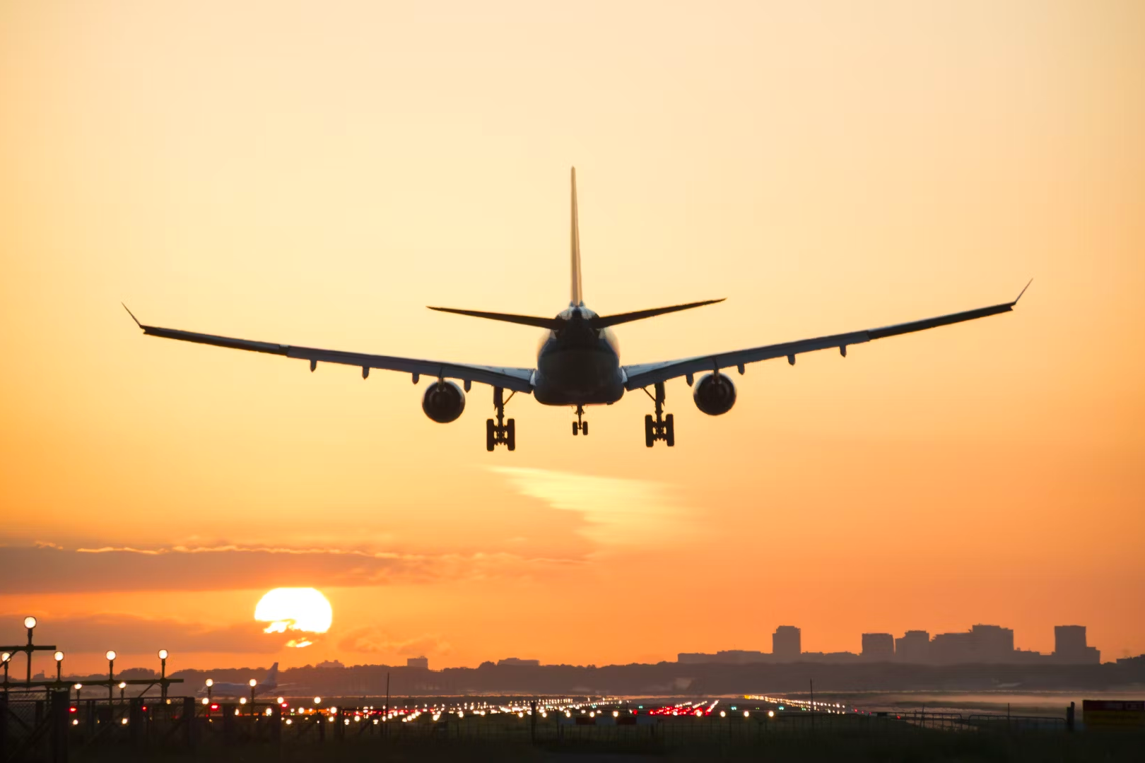 A silhouette of an aircraft about to land at sunset.