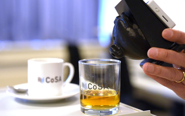 a hand holds a device over a glass containing a translucent brown liquid